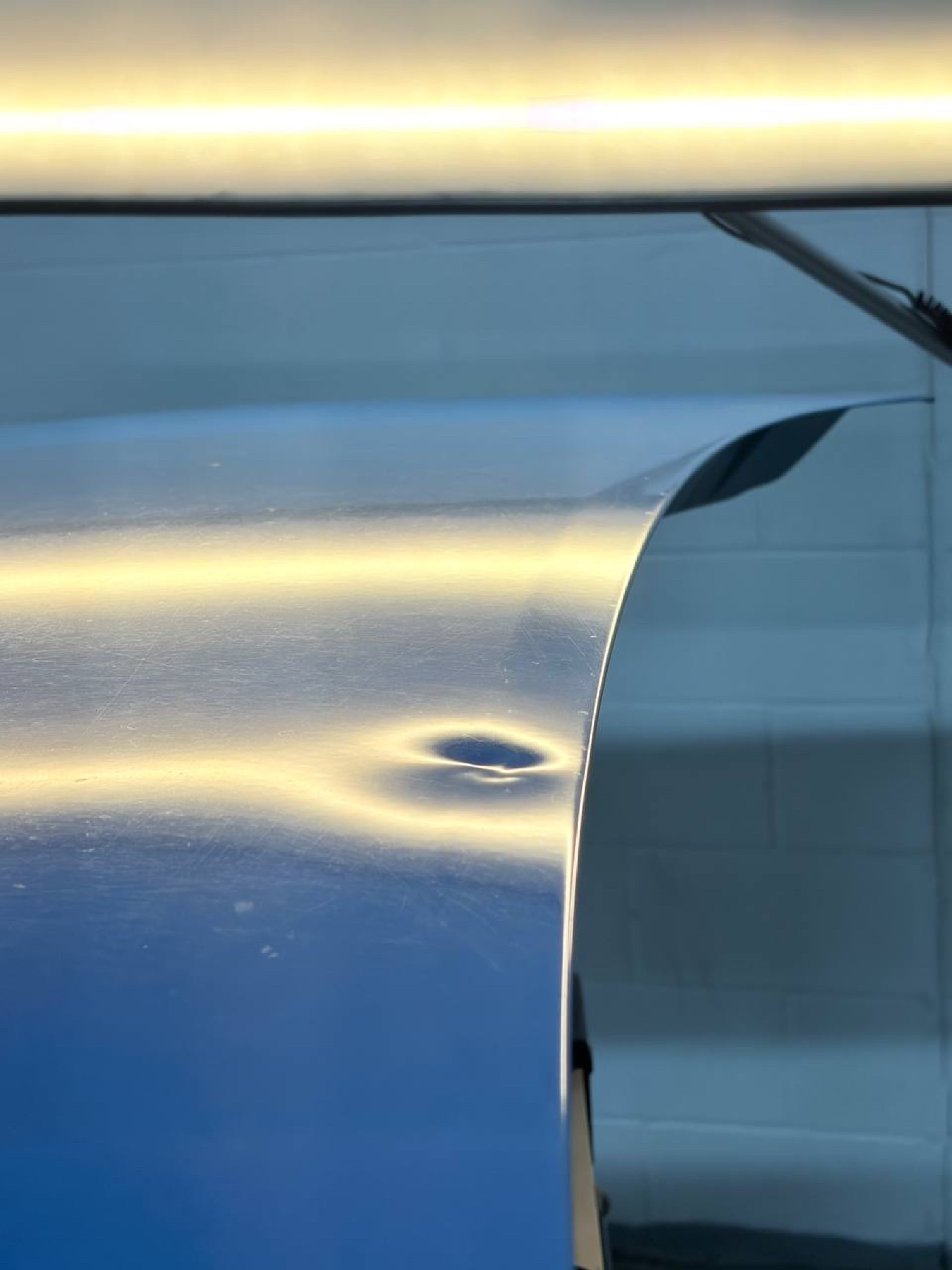 Blue vehicle quarter-panel crease before paintless dent repair, close view
